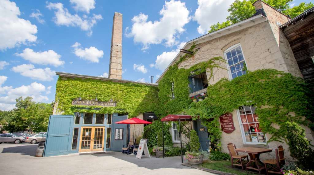Ivy-covered brick buildings with a tall chimney against a blue sky at Cedarburg.